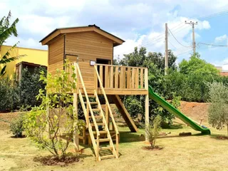 Casa de madeira suspensa integrada a um playground, com escorregador e área de brincar
