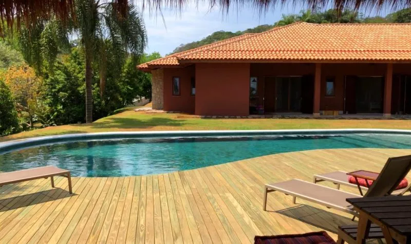 Deck de madeira contornando uma piscina residencial, com espreguiçadeiras e a casa ao fundo