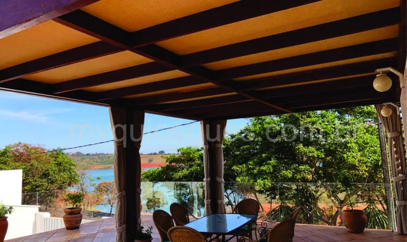 Pergolado forrado com palha castanho buclê, com mesa e cadeiras logo abaixo